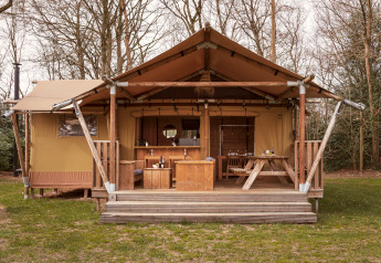 Tenda safari con veranda in legno e tavolo esterno, immersa nella natura e circondata dagli alberi.