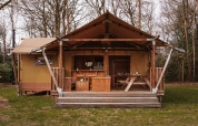Safari-Zelt mit Holzveranda und Sitzgelegenheiten im Freien, umgeben von Bäumen und Natur.