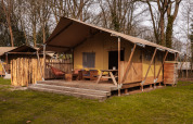 Safari-Zelt De Bos Tent auf der Gooise Heide in den Niederlanden mit Holzterrasse im bewaldeten Gebiet.