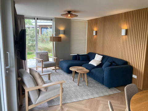 Modern living room at Duinvilla, EuroParcs Texel, with blue sofa, wooden wall panels and garden view windows.