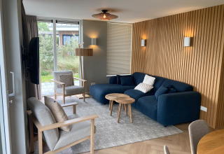 Modernes Wohnzimmer in der Duinvilla bei EuroParcs Texel, mit blauer Couch, Holzverkleidung und Gartenblick.