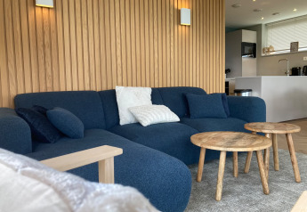 Salón moderno en Duinvilla de EuroParcs Texel con sofá azul, mesas de madera y pared de paneles.