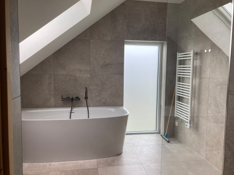 Modernes Badezimmer mit freistehender Badewanne, Dachschräge und Fenster in der Duinvilla, EuroParcs Texel.