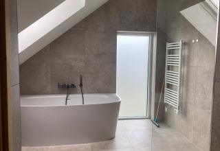Moderne badkamer met losstaand bad, schuine wand, raam en radiator in Duinvilla, EuroParcs Texel.