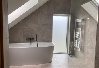 Modernes Badezimmer mit freistehender Badewanne, Dachschräge und Fenster in der Duinvilla, EuroParcs Texel.