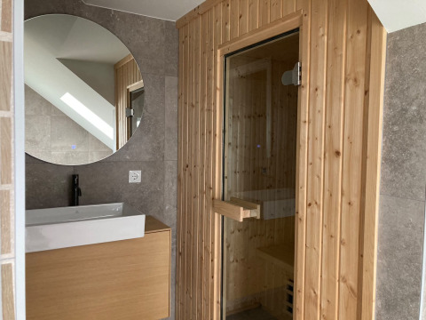 Modernes Badezimmer mit rundem Spiegel, Waschbecken und Holzsauna in der Duinvilla, EuroParcs Texel.