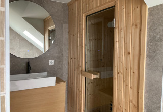 Modern bathroom interior with round mirror, sink and wood sauna at Duinvilla, EuroParcs Texel, Netherlands.