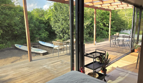 Udsigt fra Slowlodge Echo ved Zomerlicht i Holland med terrasse, surfbrætter og natur udenfor.