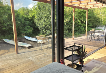 Udsigt fra Slowlodge Echo ved Zomerlicht i Holland med terrasse, surfbrætter og natur udenfor.