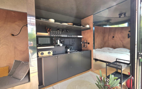 Modern lodge interior with compact kitchen and bedroom, featuring wood panels at Slowlodge Echo, Zomerlicht.