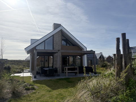 Modern lodge named Duinvilla Wellness with large windows and covered terrace in a scenic natural setting.