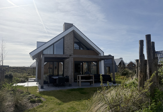 Moderne lodge genaamd Duinvilla Wellness met grote ramen en een overdekt terras in een groene omgeving.