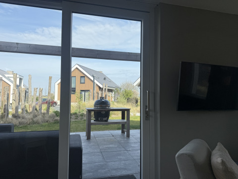 View through glass door to patio with grill and Duinvilla lodges at EuroParcs Texel, Netherlands.