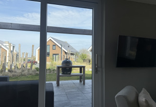 View through glass door to patio with grill and Duinvilla lodges at EuroParcs Texel, Netherlands.