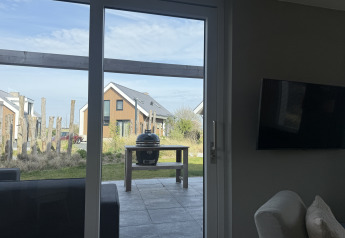 Vista a través de la puerta de cristal hacia la terraza con parrilla y lodges Duinvilla en EuroParcs Texel, Países Bajos.