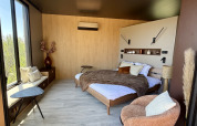 Modern lodge room at Cabane Spa Loggy with a large bed, cozy chair, big windows and natural decor.