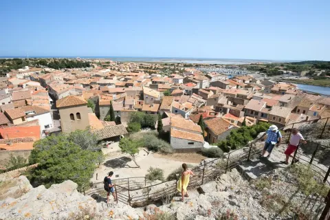 Zicht op Gruissan in Occitanië, Frankrijk met oranje daken, zee in de verte en mensen op een stenen pad.