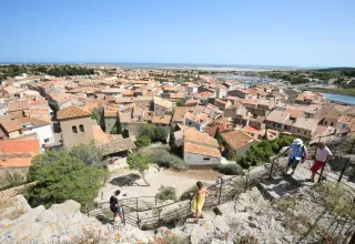 Zicht op Gruissan in Occitanië, Frankrijk met oranje daken, zee in de verte en mensen op een stenen pad.