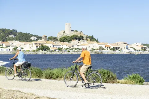 Twee fietsers aan het water met zicht op Gruissan en een oude toren in Occitanië, Frankrijk.