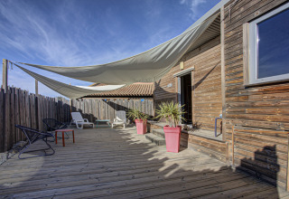 Træterrasse med solsejl, liggestole og farverige potteplanter ved en træhytte i Seasonova Camping Barberousse.