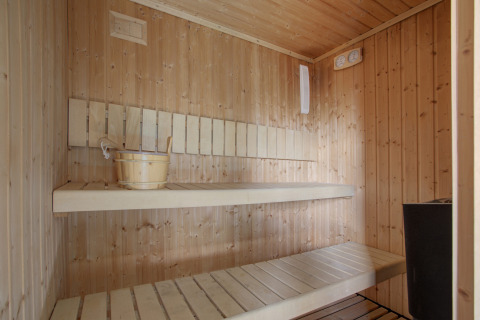 Binnenkant van een houten sauna met banken en emmer water bij Seasonova Camping Barberousse.