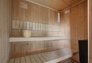 Inde i en traditionel træsauna med bænke, vandspand og varmeapparat på Seasonova Camping Barberousse.
