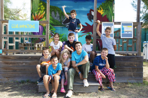 Kinderen en een volwassene met gezichtsschmink poseren aan het Club Animations-bord van Seasonova Camping Barberousse, Frankrijk.