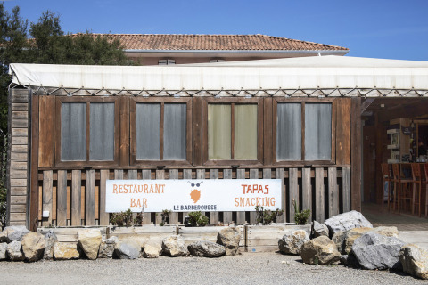 Facade af en restaurant ved Seasonova Camping Barberousse i Occitanie, Frankrig, med et skilt og træsider.