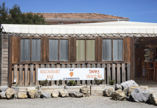 Facade af en restaurant ved Seasonova Camping Barberousse i Occitanie, Frankrig, med et skilt og træsider.