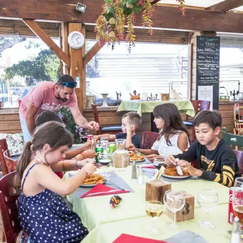 Børn sidder ved et bord og spiser mad på Seasonova Camping Barberousse i Occitanie, Frankrig.