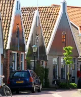 Una calle soleada en Den Hoorn, Países Bajos, con casas de tejado alto, una ciclista y farolas antiguas.