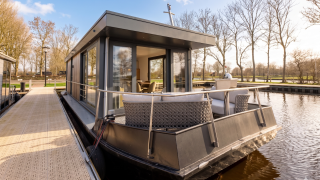 Houseboat moderno ad Offingawier con ampia terrazza esterna, vetrate e vista su acqua e alberi.