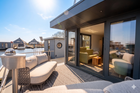 Moderne husbåd terrasse med sofa og store vinduer ved Houseboat Offingawier, Friesland, Holland, solrig dag.