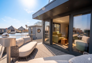 Moderne husbåd terrasse med sofa og store vinduer ved Houseboat Offingawier, Friesland, Holland, solrig dag.