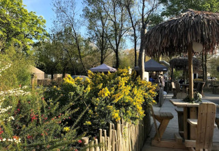 Area esterna con tavoli in legno e ombrelloni di paglia a Camping les Rives de Grand Lieu, Pays de la Loire.