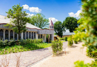 Beautiful lodge with stone walls, arched windows, and a turret, set in lush greenery on a sunny day.