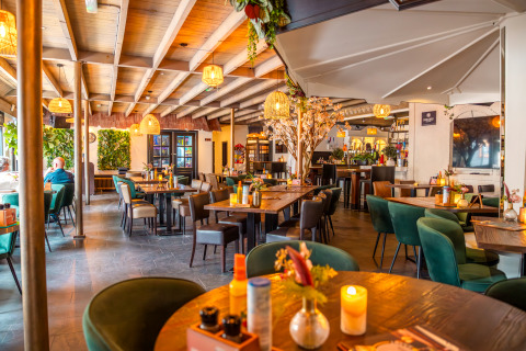 Modern lodge dining area with wooden beams, green chairs, cozy lighting, and floral table decorations.