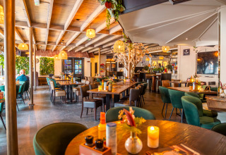 Modern lodge dining area with wooden beams, green chairs, cozy lighting, and floral table decorations.