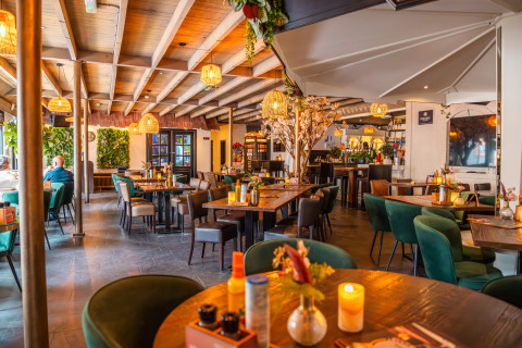 Modernes Lodge-Restaurant mit Holzbalkendecke, grünen Stühlen, Blümendekor und warmem Licht.