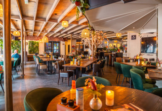 Modernes Lodge-Restaurant mit Holzbalkendecke, grünen Stühlen, Blümendekor und warmem Licht.