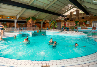 Indoor swimming pool at a lodge, children and adults swimming and playing in a tropical-themed interior.