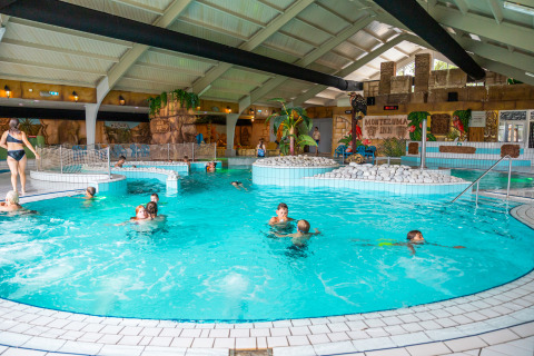 Indendørs swimmingpool med børn og voksne, legende i et tropisk tema på et feriecenter eller lodge.