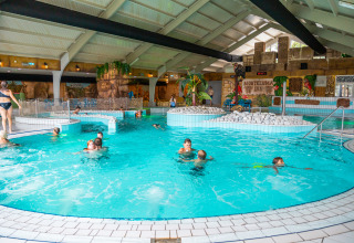Indendørs swimmingpool med børn og voksne, legende i et tropisk tema på et feriecenter eller lodge.
