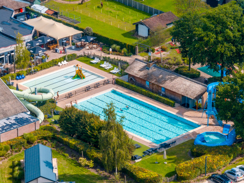 Aerial view of a lodge featuring outdoor swimming pools, waterslides, loungers, and lush surrounding greenery.