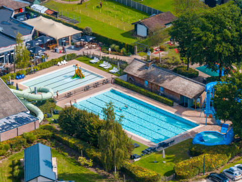 Luftfoto af en lodge med udendørs swimmingpool, rutsjebaner og afslapningsområder omkranset af natur.