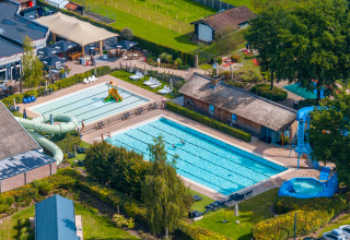 Luftfoto af en lodge med udendørs swimmingpool, rutsjebaner og afslapningsområder omkranset af natur.