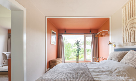Slaapkamer in Tiny House XL bij De Kremmer, Nederland, met oranje nis en groot raam met natuurzicht.
