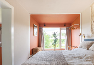Slaapkamer in Tiny House XL bij De Kremmer, Nederland, met oranje nis en groot raam met natuurzicht.