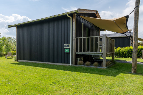 Black Tiny House XL with porch and beige awning on green lawn at De Kremmer, Netherlands, sunny day.