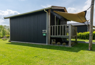 Black Tiny House XL with porch and beige awning on green lawn at De Kremmer, Netherlands, sunny day.